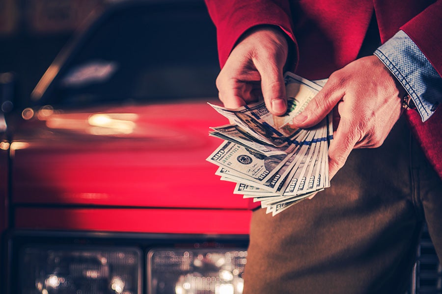 A person holding a fan of cash in front of a car